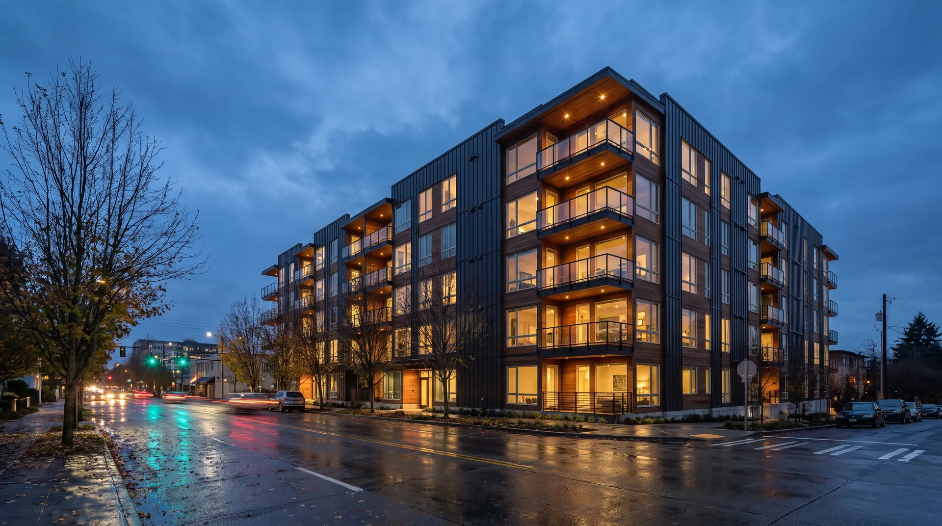 A modern mid-rise condominium building with balconies on a rain-wet street at dusk